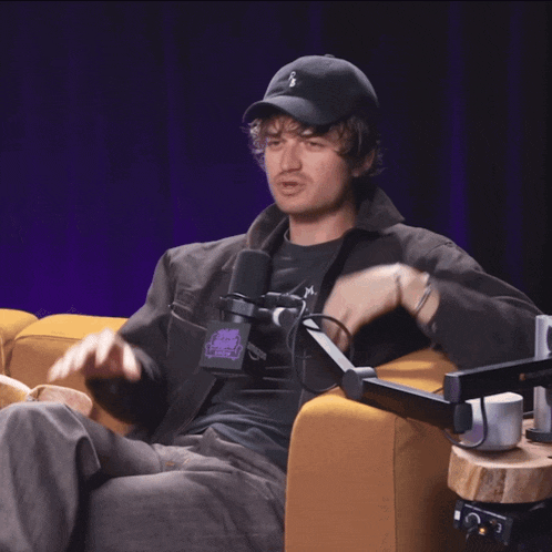 a man wearing a hat with the letter s on it sits in a chair with a microphone