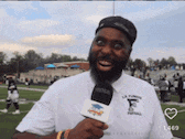 a man with a beard is holding a microphone in front of a football field .