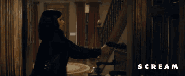 a woman holding a gun in front of a door that says scream on the bottom