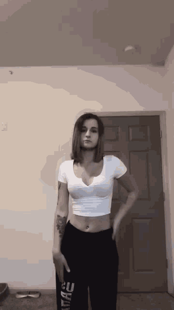 a woman in a white crop top and black sweatpants is standing in front of a door