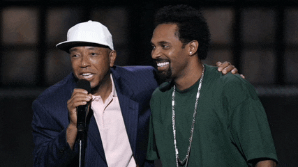a man in a white hat stands next to a man in a green shirt holding a microphone