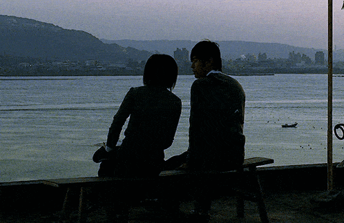 a man and woman sit on a bench looking out over a body of water