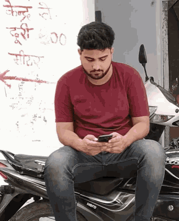 a man sits on a motorcycle looking at his cell phone