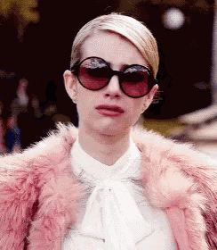 a woman wearing a pink fur coat and sunglasses is making a funny face .