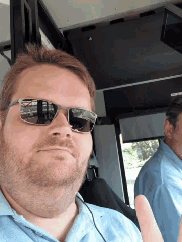 a man wearing sunglasses and a blue shirt giving a thumbs up