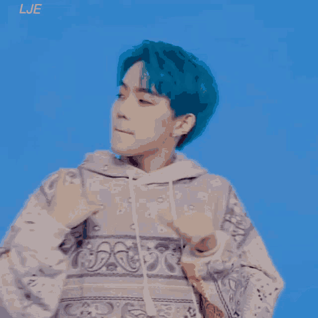 a person with blue hair is wearing a paisley sweater and giving a thumbs up