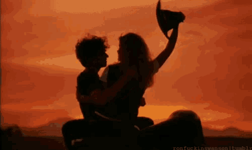 a man is holding a woman in his arms while she holds a cowboy hat in the air .