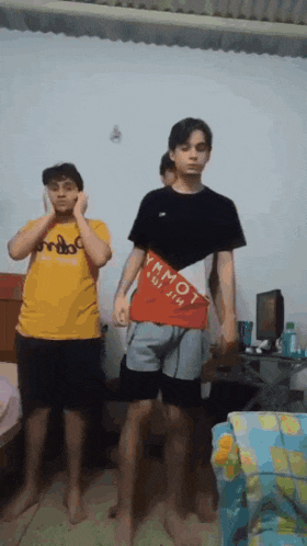 two boys are standing in a room with one wearing a shirt that says ymmot