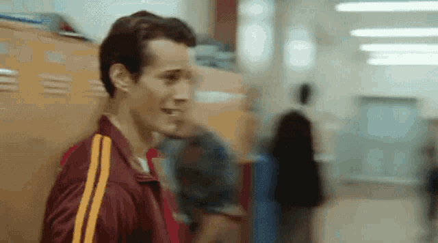 a man in a maroon shirt with yellow stripes is standing in a hallway next to lockers .