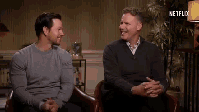 two men are sitting next to each other in chairs and talking .