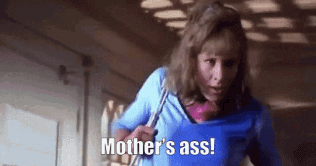a woman in a blue shirt is walking down a hallway and saying `` mother 's ass ! ''