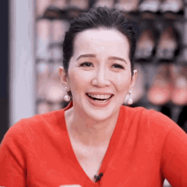 a woman wearing a red shirt and pearl earrings smiles for the camera