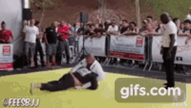 a man is wrestling another man on a yellow mat in front of a crowd of people .