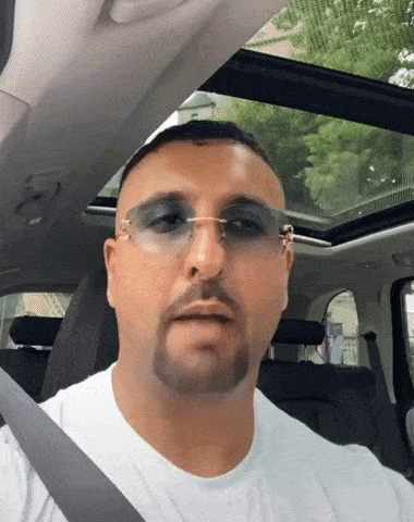 a man wearing sunglasses and a white shirt is sitting in the back seat of a car
