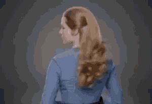 a woman in a blue shirt is standing in front of a gray background .