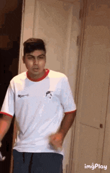 a young man in a white shirt and blue shorts is standing in a doorway .