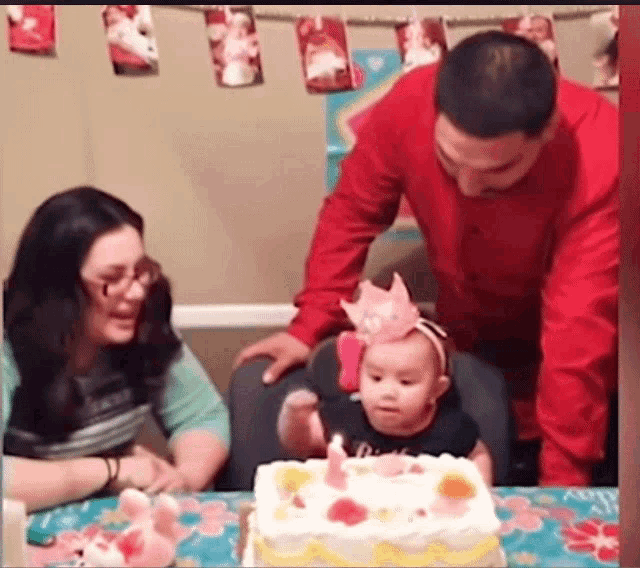 a baby is blowing out a candle on a birthday cake while a man and woman look on .