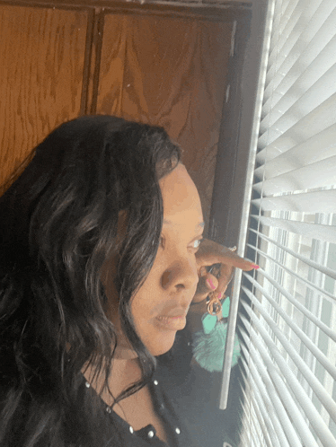 a woman looks out of a window with blinds on
