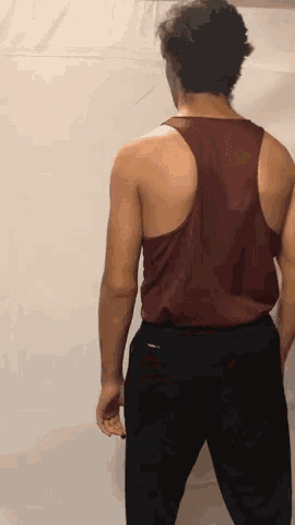 the back of a man wearing a red tank top and black pants is shown .