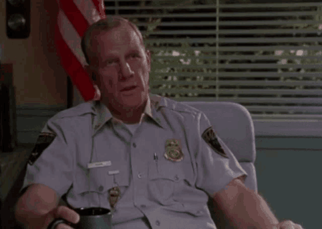 a man in a police uniform is sitting in a chair with a cup of coffee .
