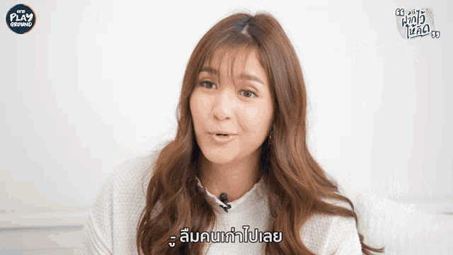 a woman in a white sweater talks into a microphone with play written on the bottom right