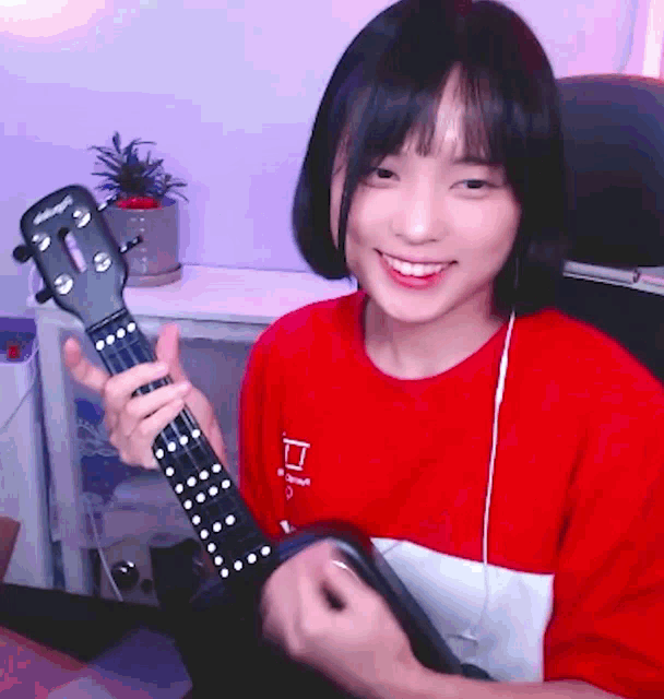 a girl in a red shirt is holding a guitar with the letter p on her shirt