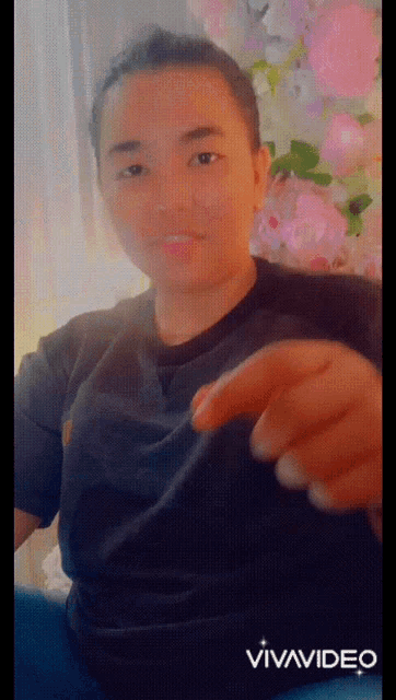 a young man in a black shirt is making a funny face in front of flowers
