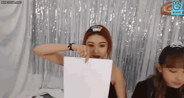 a woman with red hair is holding a piece of paper in front of her face .