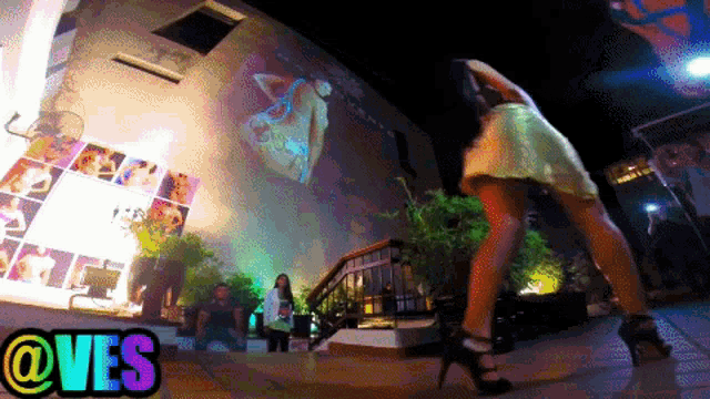 a woman in high heels stands in front of a wall that has @ves written on it