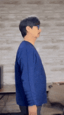 a man wearing a blue sweater and glasses is standing in front of a brick wall .