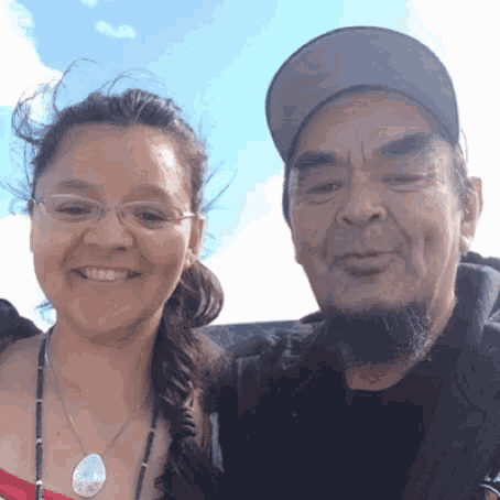 a man and a woman are posing for a picture together . the woman is wearing glasses and a necklace .