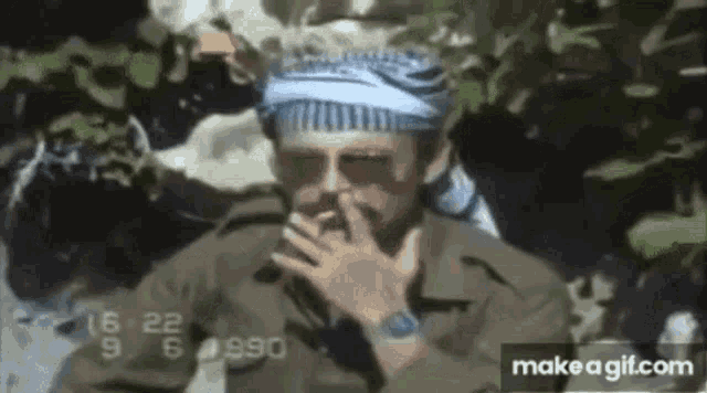 a man in a military uniform is smoking a cigarette while wearing sunglasses .