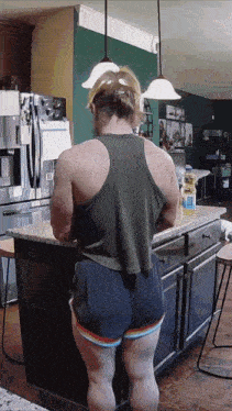 a woman is standing in a kitchen with a bottle of aquafina water on the counter