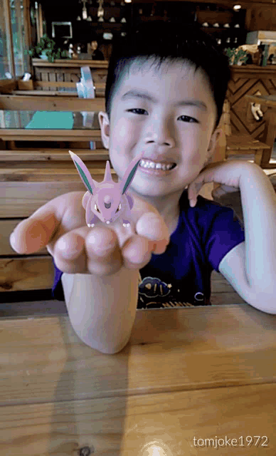a young boy is holding a pokemon in his hand and the photo was taken by tom joke 1972