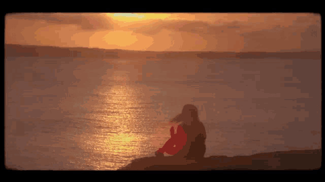 a person sitting on a cliff overlooking the ocean at sunset