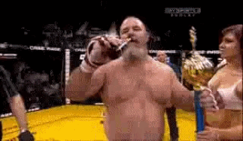a man is drinking from a bottle in a boxing ring while a woman holds a trophy