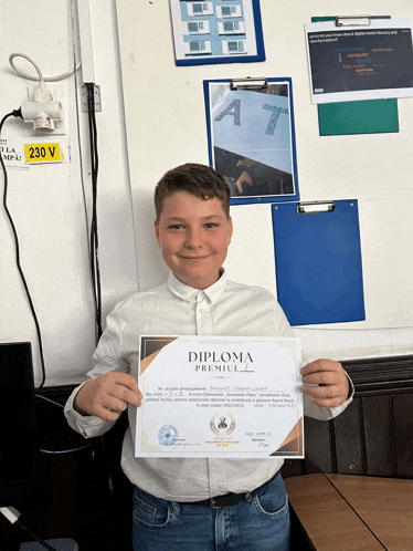 a young boy holds up a diploma in front of a white board