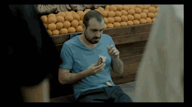 a man in a blue shirt is eating ice cream in front of a fruit stand