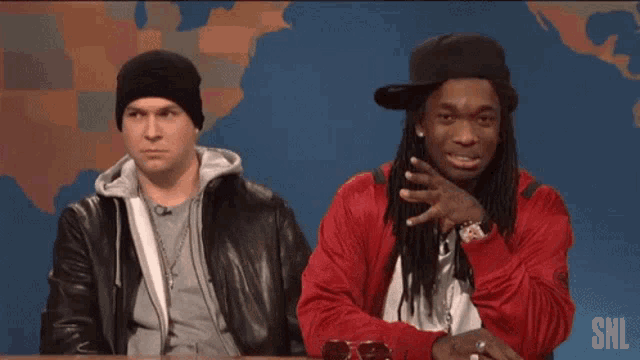 two men sitting at a table with a snl logo on the bottom