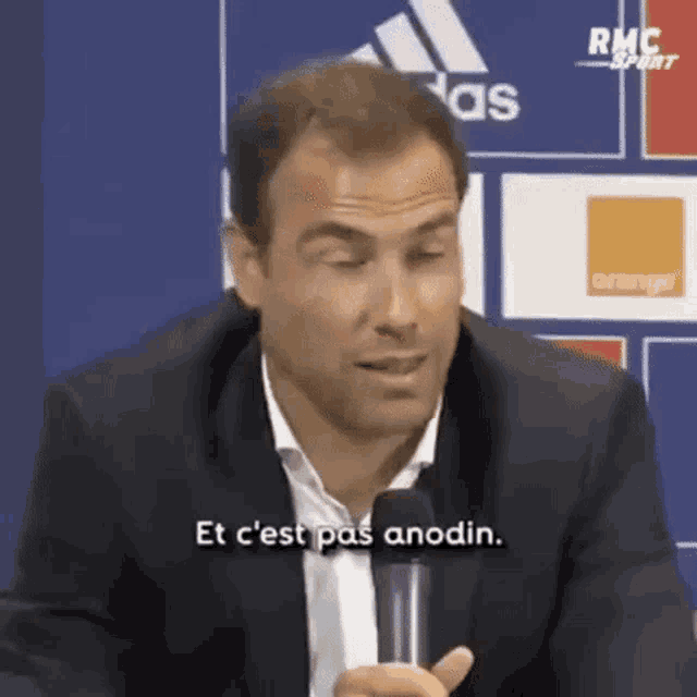 a man in a suit is talking into a microphone and says et c 'est pas anodin .