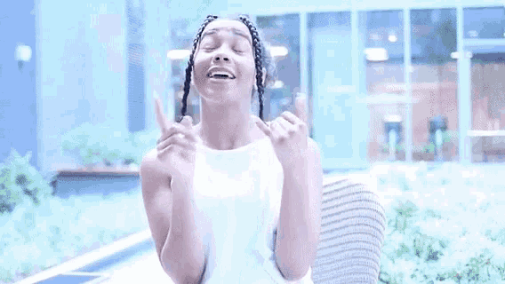 a woman with braids in her hair is sitting on a chair with her hands folded and making a funny face .