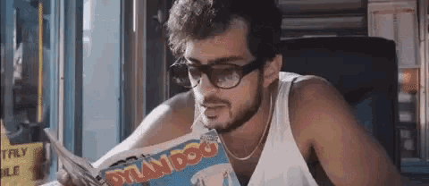 a man wearing glasses is reading a magazine .