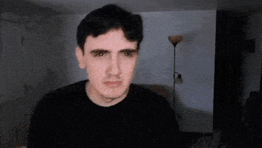 a man in a black shirt is making a funny face in a living room with a lamp in the background .