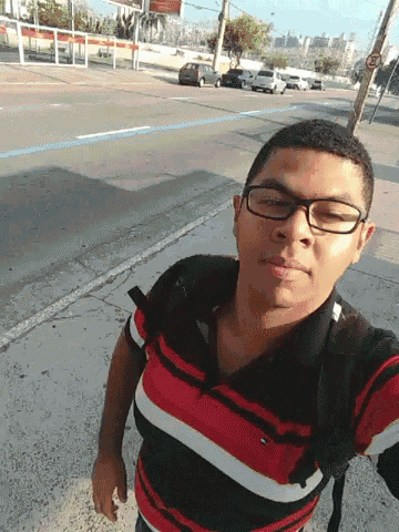 a young man wearing glasses and a red and black striped shirt is taking a selfie