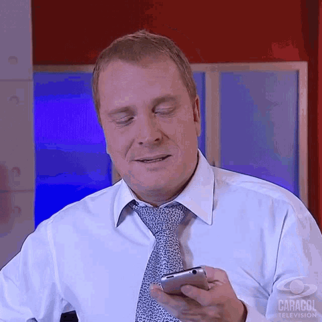 a man wearing a white shirt and tie is holding a cell phone with caracol television written on the bottom