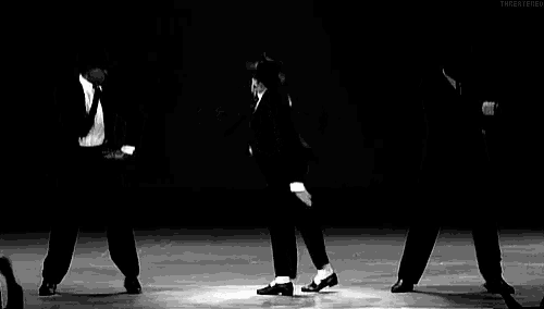 a black and white photo of a man in a suit and tie dancing on a stage with two other men .