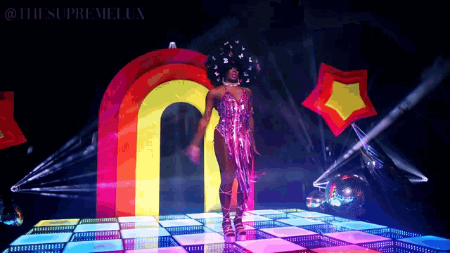 a woman is dancing on a dance floor with a rainbow arch in the background