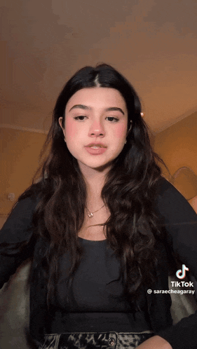 a woman with long dark hair is wearing a black shirt and a necklace