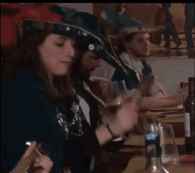 a woman wearing a feathered hat sits at a table with a man holding a glass of wine