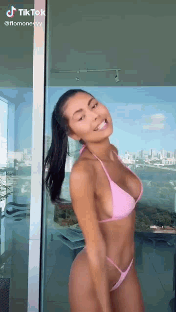 a woman in a pink bikini is standing in front of a glass door .